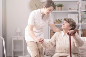 Young nurse supporting senior disabled woman with walking stick in a retirement home